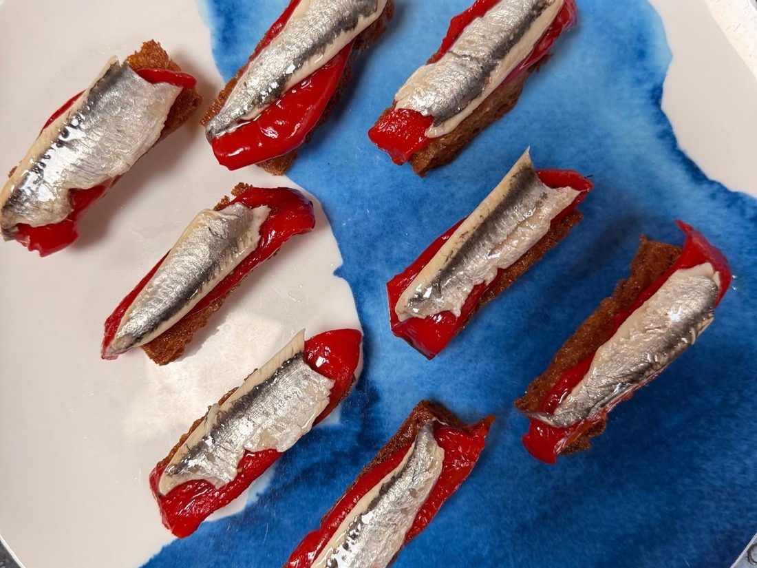 Anchovy fillets over roasted red pepper on toasted bread, plated on a blue and white splash plate