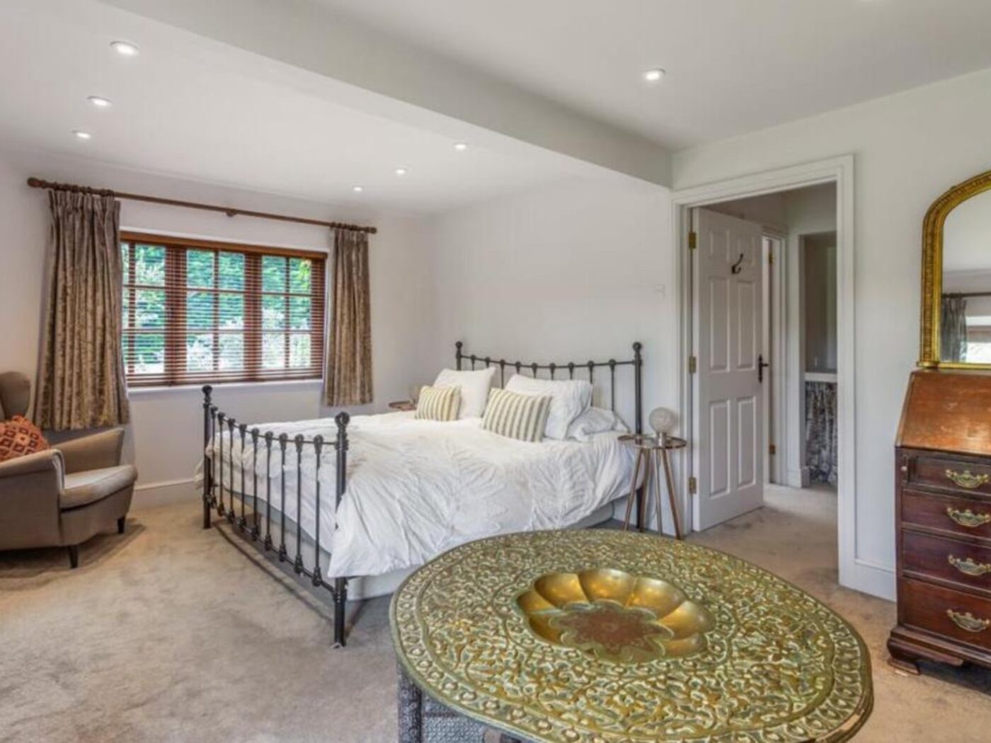 A guest bedroom with an antique brass bed, white linen and a leaded window onto greenery