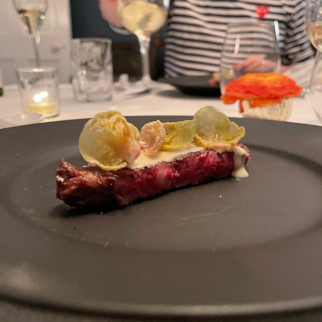Seared beef rested on a dark plate, dressed with charred brassica petals and a cream sauce