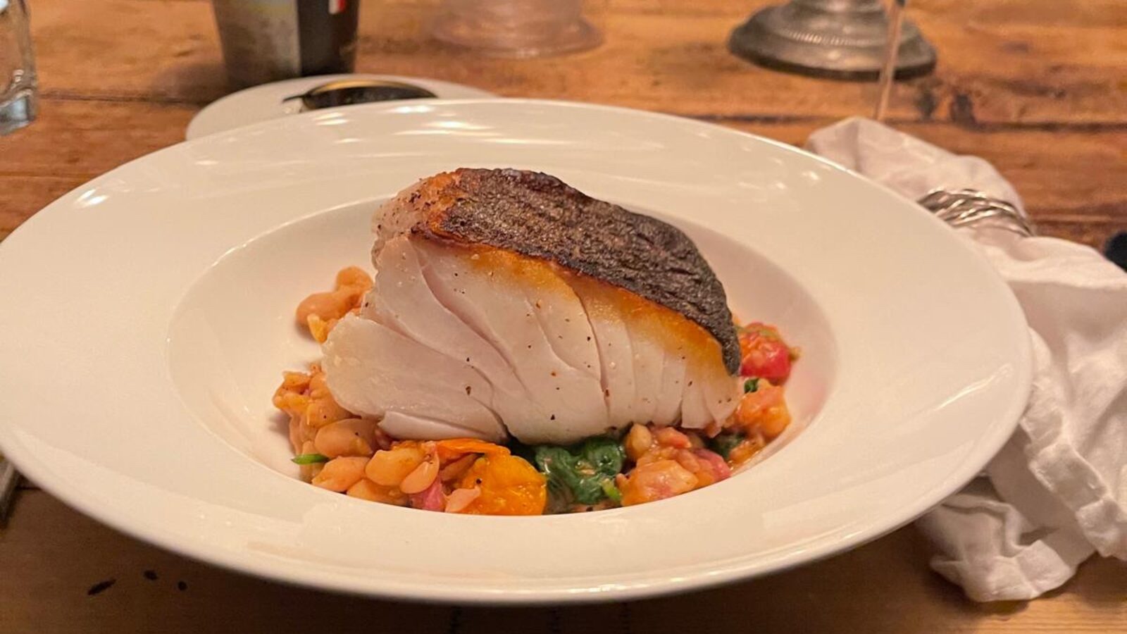 Crisp-skinned fish resting on tomatoey white beans, with a glass of white wine