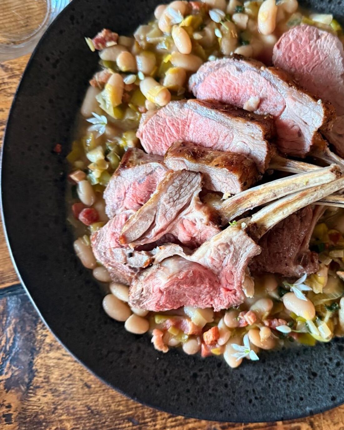Pink-roasted rack of lamb resting on braised white beans, leeks and bacon